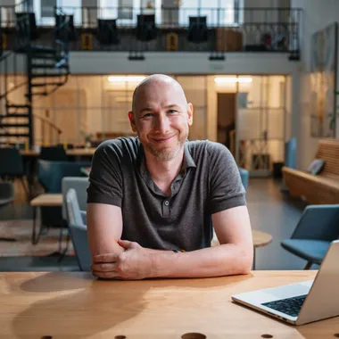 Marian Kamenistak u stolu v coworkingu, usmívá se, ruce založené.