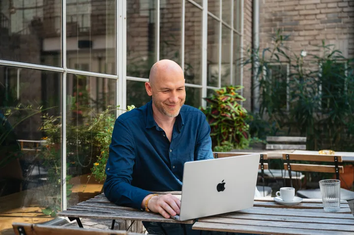 Marian Kamenistak smiling at his laptop in an outdoor courtyard.
