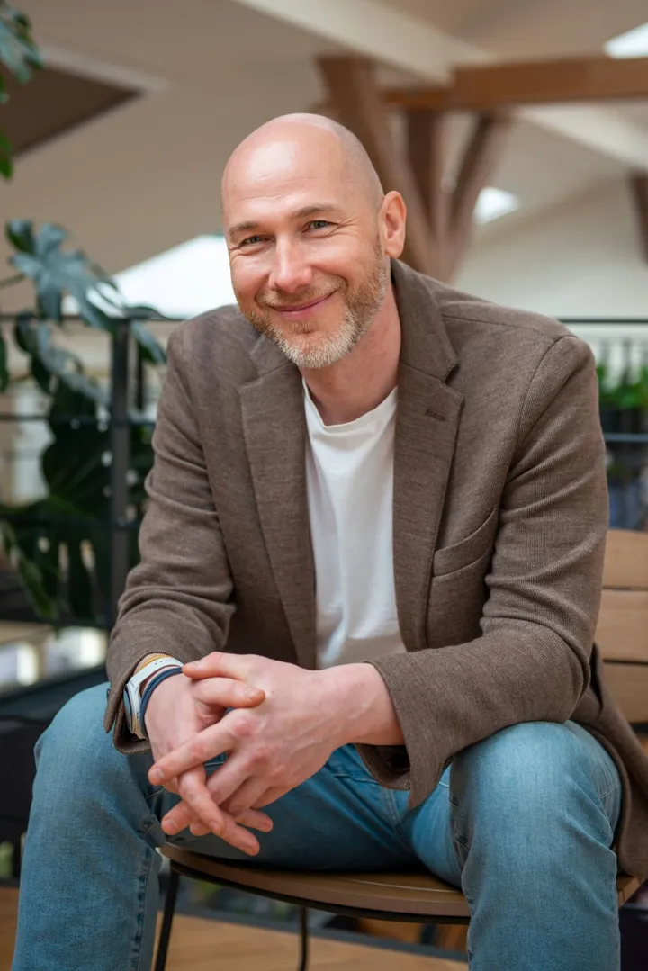 Marian Kamenistak seated, leaning forward with hands clasped, smiling.