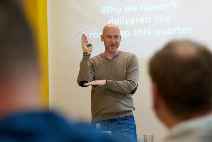 Marian Kamenistak facilitating a workshop, mid-gesture, in front of a slide about roadmap delivery.